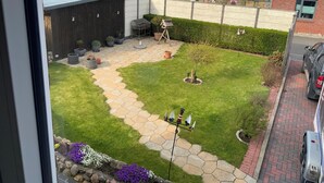 Une cour avec un chemin pavé, un petit arbre et des plantes en pot.