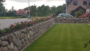 Un mur de pierres bordé d’une pelouse bien entretenue et d’une rangée de fleurs rouges.