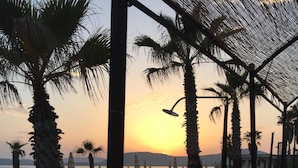 Ein Restaurant direkt am Strand mit Außenbereich, Palmen und Blick auf den Sonnenuntergang über dem Wasser.