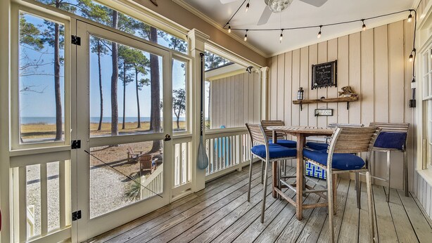 A covered outdoor area with a wooden deck, a ceiling fan, string lights, and a table with chairs.
