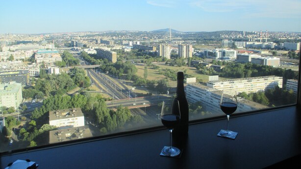 Vista de la ciudad desde una ventana, con dos copas de vino y una botella en el alféizar.