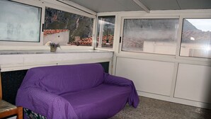 A room with a purple sofa, a small table with a plant, and a view of a mountainous landscape through large windows. - Vacation House "La Tana" (Isnello)
