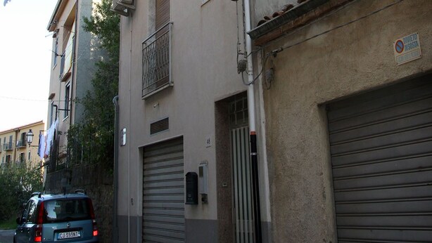 A narrow street with a building featuring a balcony and a garage door. - Vacation House "La Tana" (Isnello)