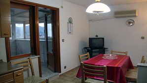 A compact living space with a dining area, a television, and a view through a sliding door. - Vacation House "La Tana" (Isnello)