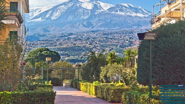 A pathway leading to a mountain with a snow-capped peak, surrounded by greenery and buildings. - SICILY ETNA SEA Beach&Pool Catania Taormina Etna District (Mascali)