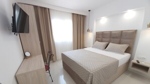 Una habitación de hotel moderna con una cama grande, un televisor de pantalla plana montado en la pared y una mesita de noche con un control remoto.