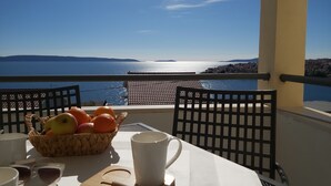 Una mesa con una cesta de fruta, una taza blanca y gafas de sol en un balcón con vistas a la costa.