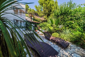 A garden area with a stone pathway, a lounge chair, and a building with a white facade.