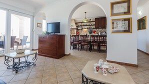 Una zona d'estar àmplia amb taula de menjador, televisió i cuina al fons.