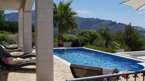 Una piscina amb vistes a les muntanyes, gandules i una zona de seients coberta.