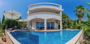A two-story building with a pool, outdoor seating, and tropical plants.