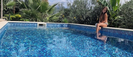 A clear blue pool surrounded by lush greenery and palm trees.