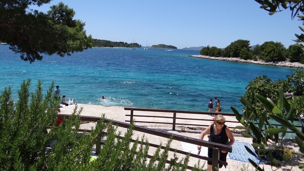A coastal view with a clear sky, a sandy beach, and a few people enjoying the water.