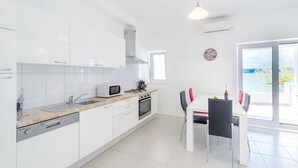 A modern kitchen with white cabinets, a microwave, a sink, and a dining area with a table and chairs. - Luxury apartment on the beach 1 (Mimice)