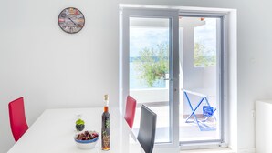 A dining area with a white table, red chairs, a decorative clock, and a view through a glass door to the outside. - Luxury apartment on the beach 1 (Mimice)