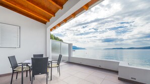 A balcony with a table and chairs, a view of the sea, and a wooden ceiling. - Luxury apartment on the beach 1 (Mimice)