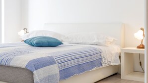 A neatly made bed with a white headboard, a blue pillow, and a white pillow. There is a bedside table with a lamp on it. - Luxury apartment on the beach 1 (Mimice)