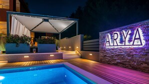 A swimming pool with a covered area, steps leading to a stone wall with the name 'ARYA' illuminated. - EXCLUSIVE VILLA ARYA private heated pool, gym, sauna, roof hot tub near the sea. (Podstrana)