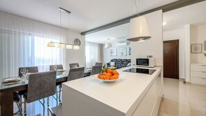 A modern kitchen with a central island, a dining area with chairs, and a living space with a sofa. - EXCLUSIVE VILLA ARYA private heated pool, gym, sauna, roof hot tub near the sea. (Podstrana)