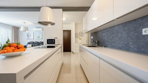 A modern kitchen with white cabinetry, a large island with a bowl of oranges, a microwave, and a grey backsplash. - EXCLUSIVE VILLA ARYA private heated pool, gym, sauna, roof hot tub near the sea. (Podstrana)
