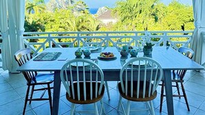Un espacio comedor al aire libre techado con una mesa dispuesta para cuatro, sillas blancas y un ventilador de techo.