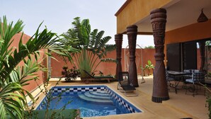 A pool area with a checkered tile edge, surrounded by plants and a wooden pergola. - Charming recent air-conditioned 3 bedroom villa with swimming pool  (Ngaparou)