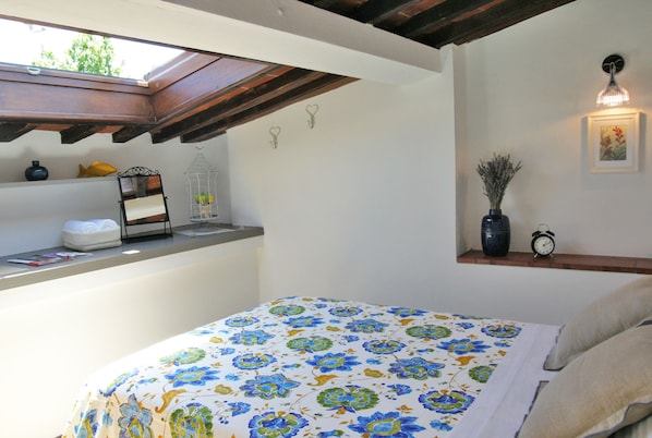 A bedroom with a bed, a skylight, a shelf with decorative items, and a wall-mounted light fixture.
