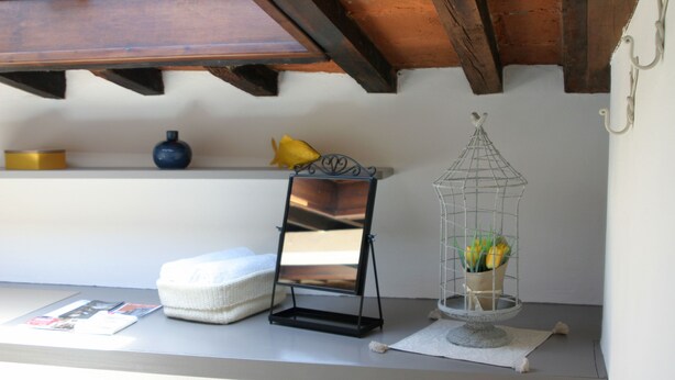 A shelf with a blue vase, a yellow decorative item, a black mirror stand, and a wire birdcage with flowers. - Santa Croce Studio in the historic center (Firenze)