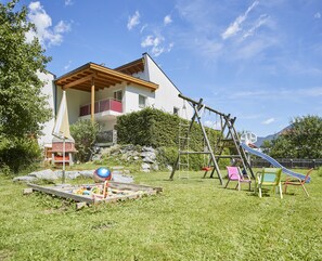 Uma casa de dois andares com um deck de madeira, balanço e escorrega no quintal.