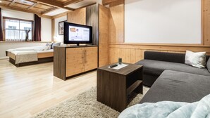 A modern living room with a wooden ceiling, a television on a wooden cabinet, a sofa, and a bed. - Apart amber with 135 m² with a large sunny terrace for 6-11 people (Ried im Oberinntal)