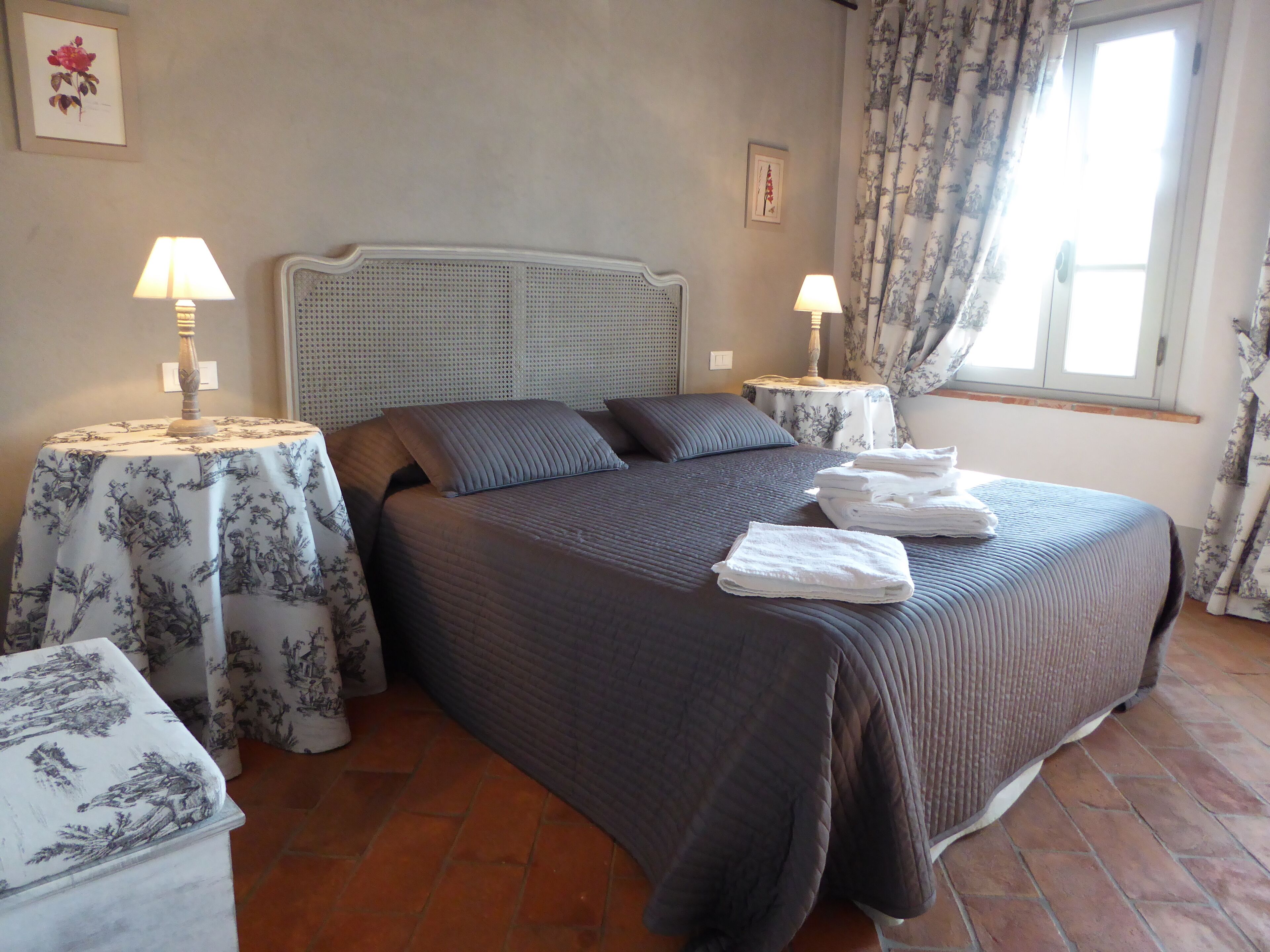 A neatly made bed with a headboard, two bedside tables with lamps, and a window with curtains.