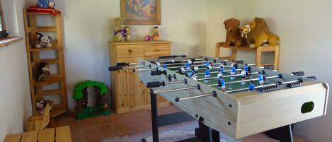 A room with a foosball table, a wooden shelf with stuffed animals, a ladder, and a painting on the wall.