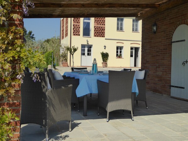 An outdoor patio with wicker furniture, a table set for dining, and a building with a brick facade in the background.