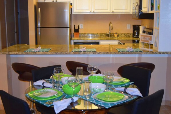 Comedor con una mesa dispuesta para seis personas, una cocina al fondo y un cartel que dice 'WELCOME'.