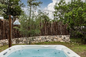 Un bain à remous dans un jardin, avec un mur en pierre et une clôture en bois, le tout entouré d’arbres.