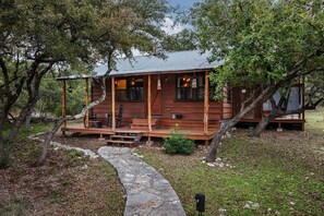 Un chalet rustique doté d’une véranda, d’un chemin en pierre et entouré d’arbres.