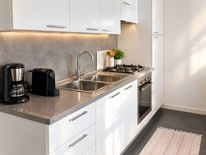 Una cocina moderna con un lavamanos de acero inoxidable, una cafetera, una estufa y armarios blancos.