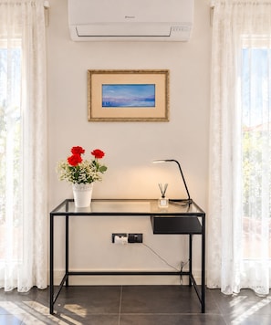 Una habitación con escritorio, un cuadro enmarcado, un florero con flores y un equipo de aire acondicionado.