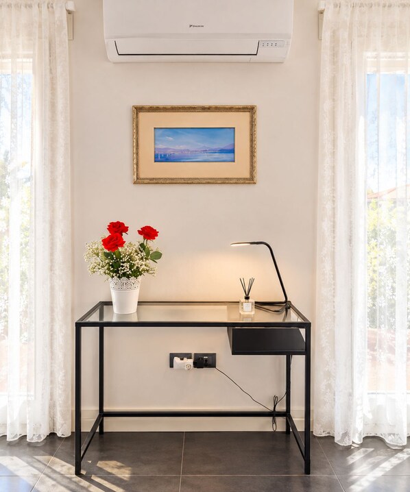 Una habitación con escritorio, un cuadro enmarcado, un florero con flores y un equipo de aire acondicionado.