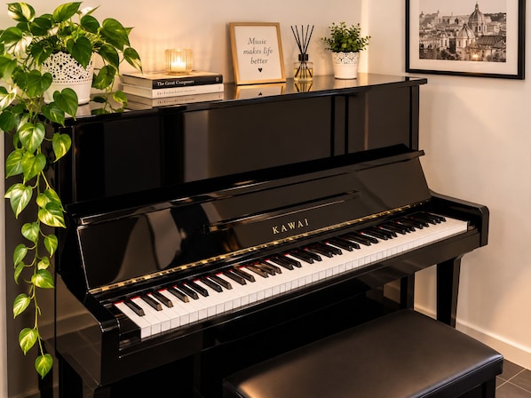 A black Kawai upright piano with a bench, surrounded by decorative items including books, a candle, and a framed quote.