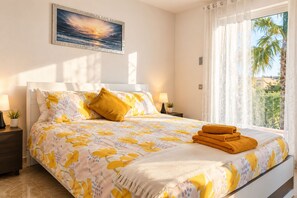 Una camera d'albergo con un letto, un comodino, una lampada, un quadro e vista su palme.