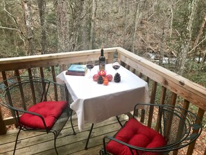 A wooden deck with a table set for two, featuring books, wine glasses, candles, and pinecones. - Stream-Side Guesthouse In beautiful Rawley Springs (Hinton)