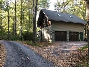 A two-story cabin with a garage, surrounded by a forested area. - Stream-Side Guesthouse In beautiful Rawley Springs (Hinton)
