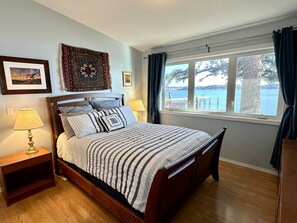 Un dormitorio con cama de madera, una mesita de noche con lámpara, una ventana con vista a un lago y un tapiz en la pared.