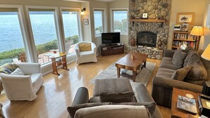 Ein Wohnzimmer mit Kamin aus Stein, einem Fernseher und Blick auf das Wasser.