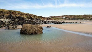 A beach with clear water, a large rock in the center, and a sandy shore. - 5-Bed Coastal Retreat w/ Studio, Sauna & Sea Views (Newgale)