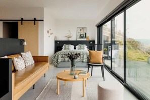 Une chambre à coucher moderne, équipée d’un lit, d’un canapé, d’un fauteuil et d’une grande fenêtre donnant sur l’extérieur.