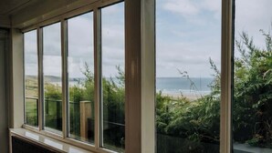 A room with large windows overlooking a garden and a beach. - 5-Bed Coastal Retreat w/ Studio, Sauna & Sea Views (Newgale)