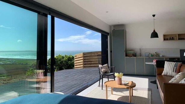 A modern living room with a large sliding glass door leading to a balcony overlooking the ocean. - 5-Bed Coastal Retreat w/ Studio, Sauna & Sea Views (Newgale)
