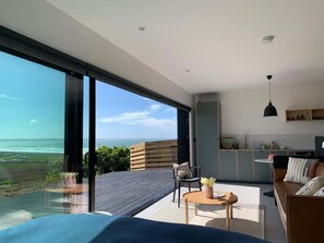 A modern living room with a large sliding glass door leading to a balcony overlooking the ocean. - 5-Bed Coastal Retreat w/ Studio, Sauna & Sea Views (Newgale)
